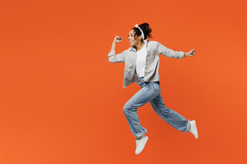 Fototapeta na wymiar Full body side view young woman of African American ethnicity she wears grey shirt headband jump high run fast hurrying isolated on plain orange background studio portrait. People lifestyle concept.