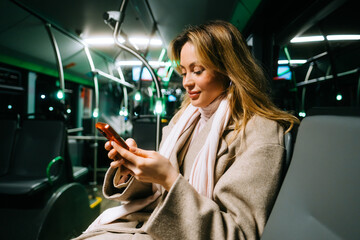 An attractive caucasian woman using a smartphone while riding a bus in the night. Young beautiful...