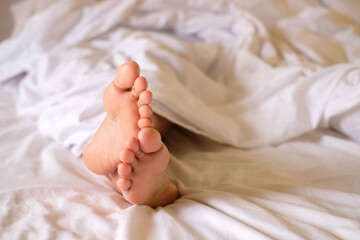 Two feet of woman awake on mattress and white blanket, morning photo, health care concept