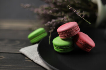 traditional American macaroons in pink and bright green color on a wooden background and a black plate next to purple fragrant flowers