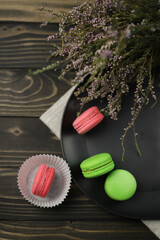 traditional American macaroons in pink and bright green color on a wooden background and a black plate next to purple fragrant flowers
