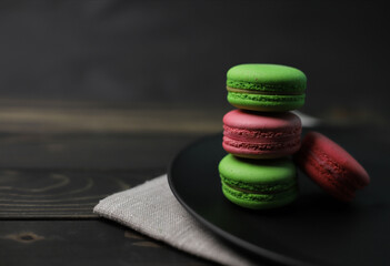 traditional American macaroons in pink and bright green color on a wooden background and a black plate next to purple fragrant flowers