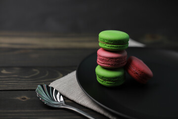 traditional American macaroons in pink and bright green color on a wooden background and a black plate next to purple fragrant flowers