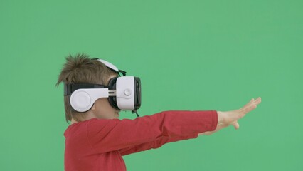 Child with virtual reality glasses looking around, surprised, green background
