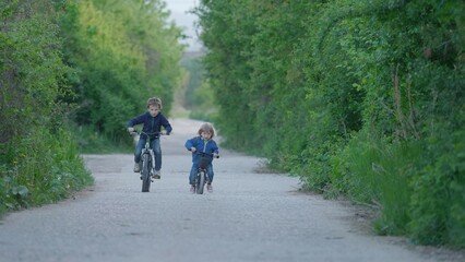 Brother riding bicycles on empty village road, children unequal competition