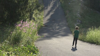 Little child with back ride on scooter on big valley, have fun in nature