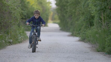 Child riding a bicycle on forest path with green trees, free childhood