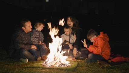 Family with three children singing at campfire in night, happy holiday in nature