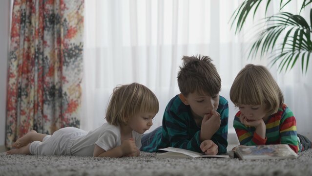 Three brothers lying on carpet and reading a book