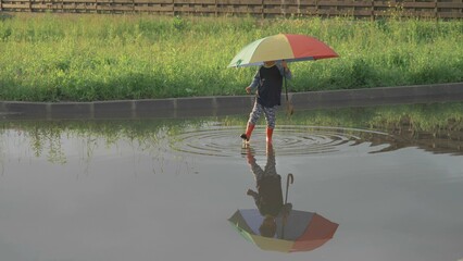 Little child standing in a puddle  with colored umbrella, little boy reflect