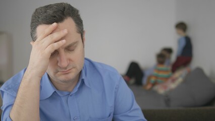 Man with headache foreground focus, careless family blur background
