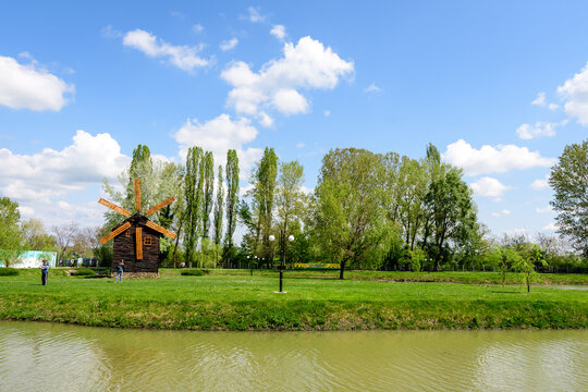 Small lake with a woodmill and an island from Chindiei Park (Parcul Chindiei) in Targoviste, Romania, in a sunny spring day with white clouds and blue sky