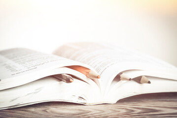 Book with colorful bookmarks with pencils on a wooden table with place for text