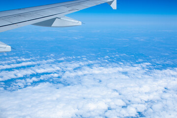 Wing of an airplane flying over white clouds and blue sky
