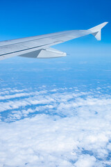 Fototapeta na wymiar Wing of an airplane flying over white clouds and blue sky