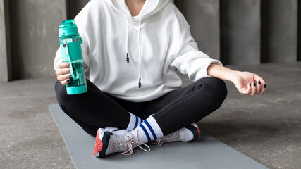 The athlete is resting after training, sitting on the mat and holding a reusable sports bottle with...