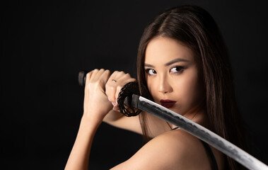 Beautiful asian woman portrait with katana samurai sword on a dark background with copy space.