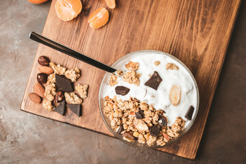 Granola cereal oatmeal with white yogurt, chocolate, fruist and nuts in a bowl on dark wooden board, top view