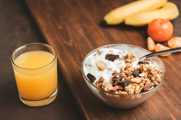 Granola cereal oatmeal with white yogurt, chocolate, banana fruit and nuts in a bowl on dark wooden board