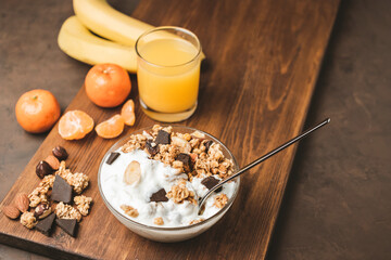 Granola cereal oatmeal with white yogurt, chocolate, banana fruit and nuts in a bowl on dark wooden board
