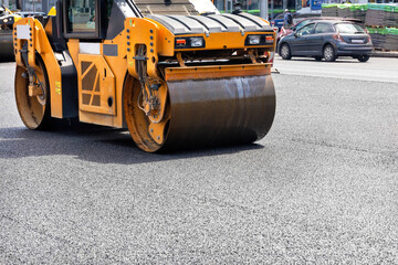 The vibrating roller rams and compacts the fresh asphalt in the middle of the carriageway on the road. - obrazy, fototapety, plakaty