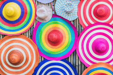 A variety of fashionable and colorful hats hanging on the bamboo backdrop of curbside shop. Women's designer hats from the sun of different colors. Design of women's beach hats. Beach hats for summer.