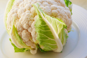 Cauliflower on a white platter with a green leaf close-up. Beautiful veins of green leaf on the head of cauliflower