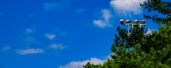 青空のゴルフ場・ティーイングエリアから見上げる空と雲と木々とナイターゴルフのライトのパノラマ（千葉県木更津市）
