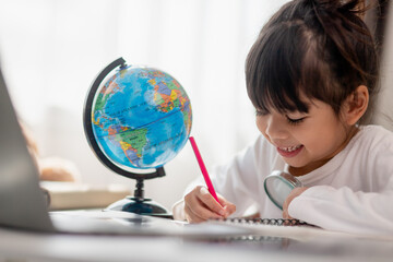 Asian schoolgirl doing her homework with laptop at home. Children use gadgets to study. Education and distance learning for kids. Homeschooling during quarantine. Stay at home