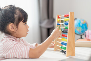 A young cute Asian girl is using the abacus with colored beads to learn how to count at home