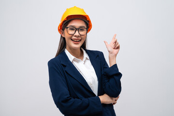 Portrait of Asian female engineer with hard hat pointing at copy space isolated on grey background.