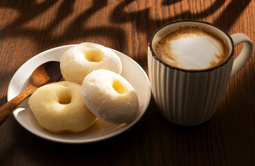 Hot latte and donuts on wooden table behind window