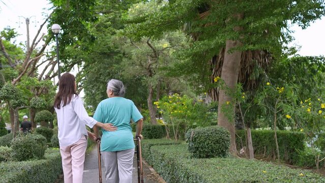 An old elderly Asian woman uses a walker and walking in the garden with her daughter.  Concept of happy retirement With care from a caregiver and Savings and senior health insurance, health care
