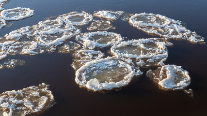 Melting, round pieces of ice and snow float down the river. Ice drift. Change of seasons. Winter, spring in Latvia.