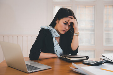 Young asian woman architect holding forehead while working on project at office desk. She is tired and tired.