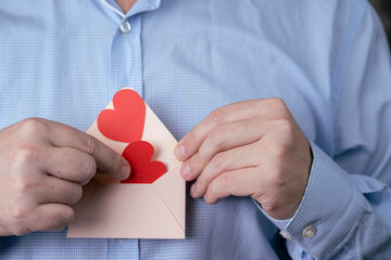 The concept of the Valentine's Day holiday. Men's hands hold an envelope with a paper heart. The...