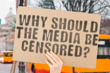 The question " Why should the media be censored? " is on a banner in men's hands with blurred background. Management. Legislation. Limited. Limitation. Dictatorship. Propaganda. Restricted