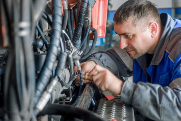 Car mechanic repairs large truck or tractor in workshop. Professional mechanic repairs truck...