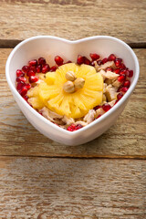Salad in a heart-shaped plate with pineapple and pomegranate n on a wooden table.
