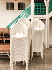 Several white plastic chairs are neatly arranged in a storage room for office supplies, shops, households. Plastic chairs are lightweight, durable, cheap and easy to store, making them popular.
