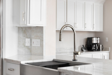 A kitchen sink detail in a white kitchen with a bronze faucet, stainless steel farmhouse sink, and...