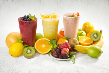 Vasos de batidos diversos de frutas saludables, con frutas alrededor sobre textura de madera sutil en fondo blanco con espacio de fondo en blanco