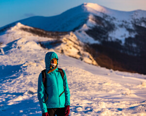 Fototapeta na wymiar backpacker girl walks along the top of a snowy ridge during sunset in the mountains, colorful winter sunset seen from the top of the Beechwood Berdo Mountain
