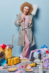 Positive housewife with curly hair does domestic work at home house cleanup cleans messy room...