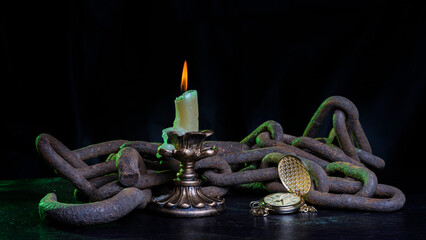 A burning candle in chains on a wooden table and a clock that has stopped time.