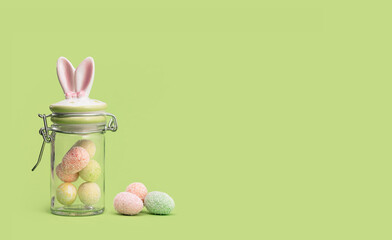 Easter bunny ears sweets jar with many tiny eggs in and near on spring yellow green edgeless...