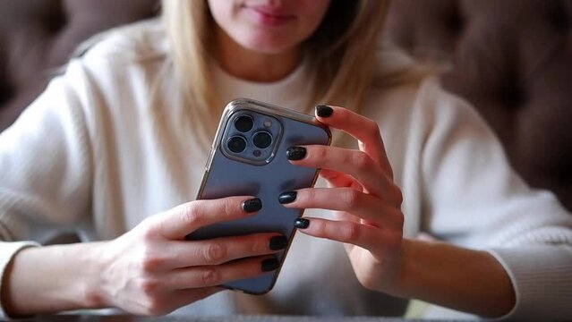  Woman hand is holding and touching iphone 13 pro and looking at the screen of mobile phone in light room.