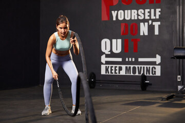 Fototapeta na wymiar athletic young woman doing exercises with battle rope in the gym