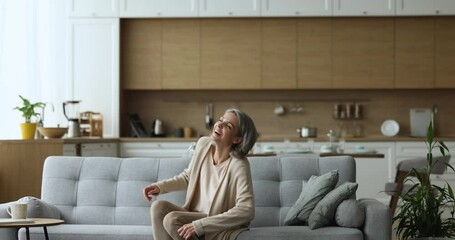 Happy carefree middle-aged female falling on cozy couch, smile enjoy comfort leisure at modern home with climate, control air-conditioning system. Stress-free weekend, relaxation, homeowner pastime