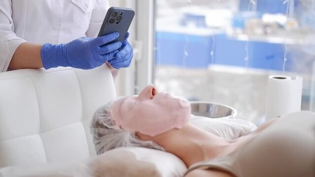 A cosmetologist takes pictures on mobile phone of a patient in a spa salon.